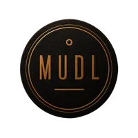 The Mudl coaster mark: a matte black coaster stamped in copper foil, reading MUDL inside a double ring, with a single dot above the wordmark and a short rule beneath it.